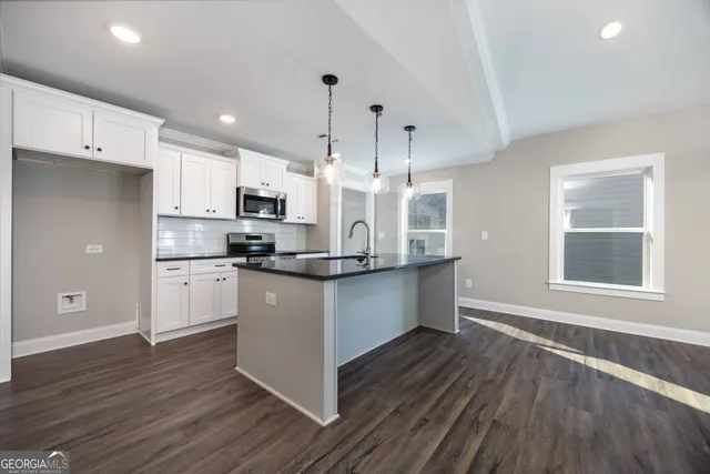 a kitchen with stainless steel appliances kitchen island granite countertop a stove a sink and white cabinets with wooden floor