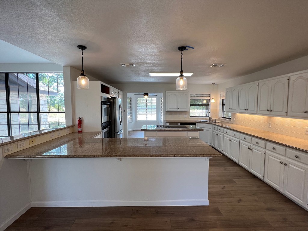 a large kitchen with granite countertop a large counter top a sink stainless steel appliances and cabinets