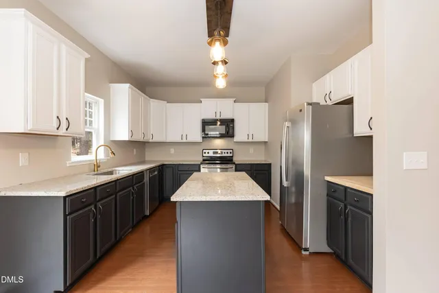 a kitchen with granite countertop a refrigerator a sink dishwasher a stove and white cabinets with wooden floor