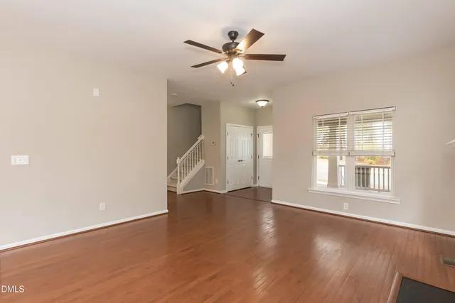 an empty room with wooden floor fan and windows