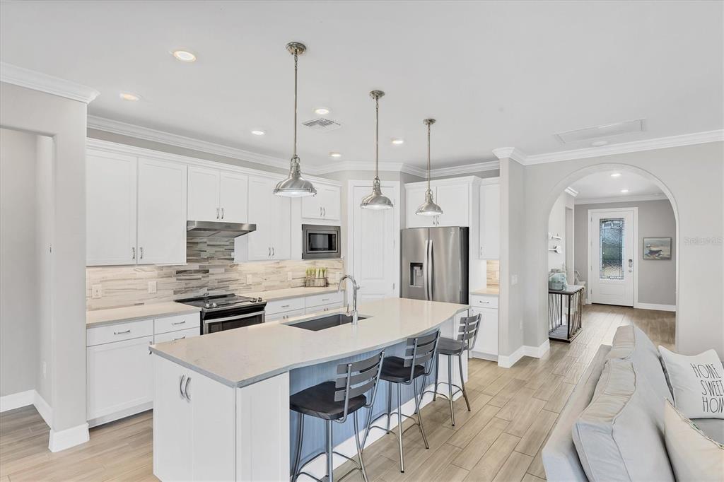 13057 Rinella Street Venice, FL 34293 - Photo 34 of 85 a kitchen with stainless steel appliances kitchen island granite countertop a stove a sink a refrigerator and white cabinets with wooden floor