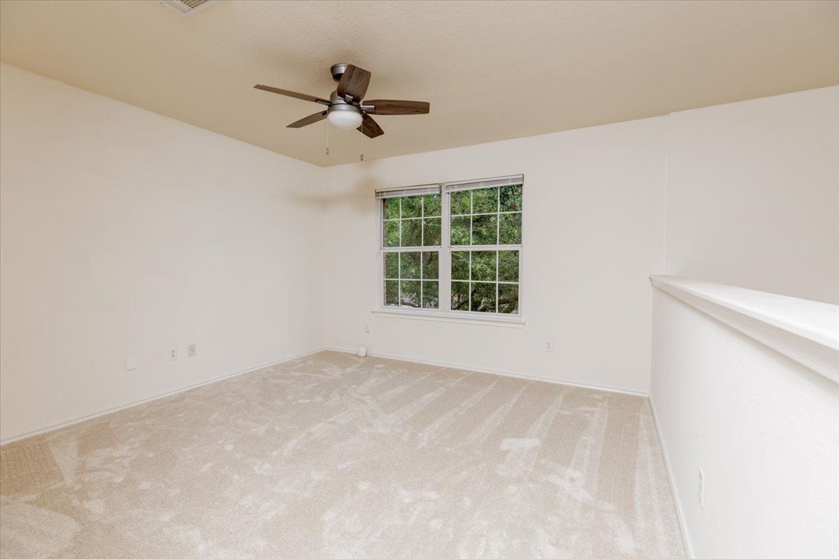 7136 Ridge Oak Road Austin, TX 78749 - Photo 18 of 28 A quiet loft space features soft carpeting, a refreshing ceiling fan, and a serene window view of lush greenery.