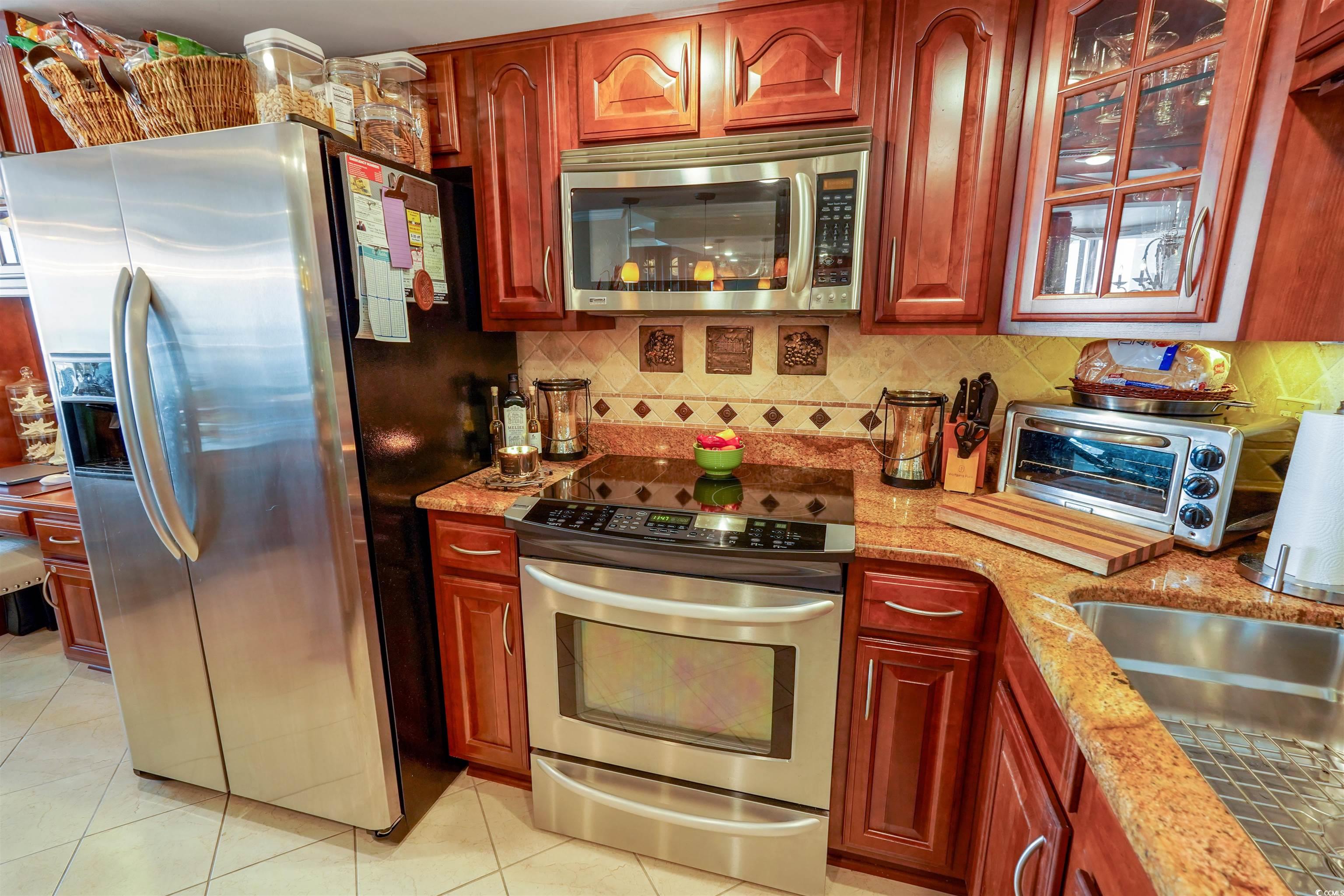 1012 North Waccamaw Drive, Unit 305 Murrells Inlet, SC 29576 - Photo 18 of 38 Kitchen with appliances with stainless steel finishes, light tile patterned floors, light stone countertops, backsplash, and dark brown cabinets