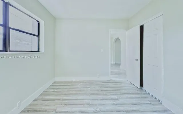 a view of an empty room with wooden floor and a window