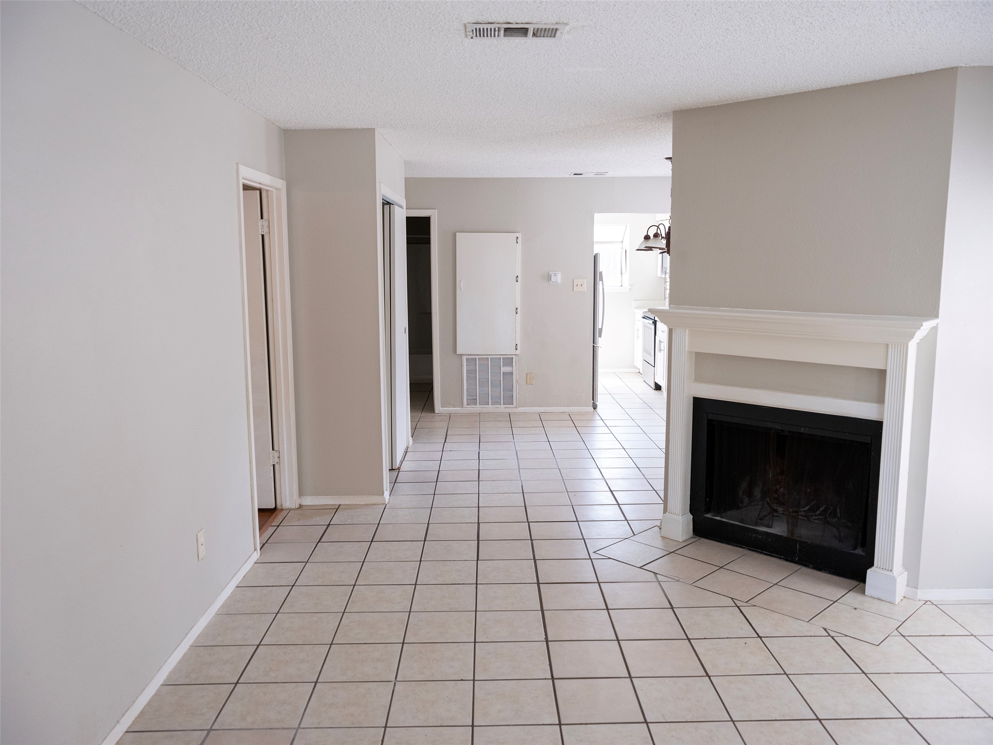 Unfurnished living room with a textured ceiling, visible vents, a fireplace, and light tile patterned floors