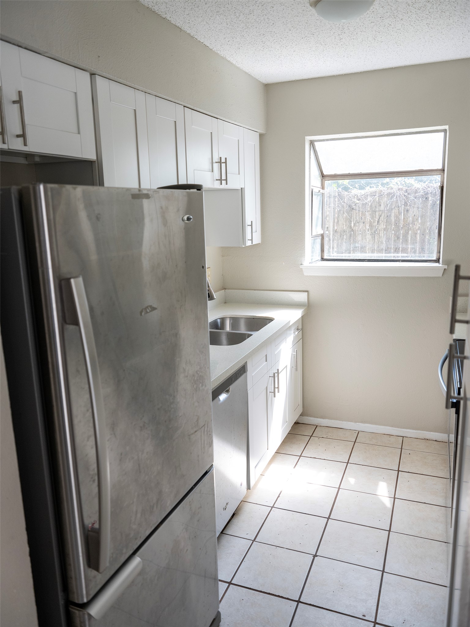 1903 West Loop, Unit B Austin, TX 78758 - Photo 12 of 15 Kitchen with white cabinetry, light tile patterned floors, a textured ceiling, a sink, and appliances with stainless steel finishes