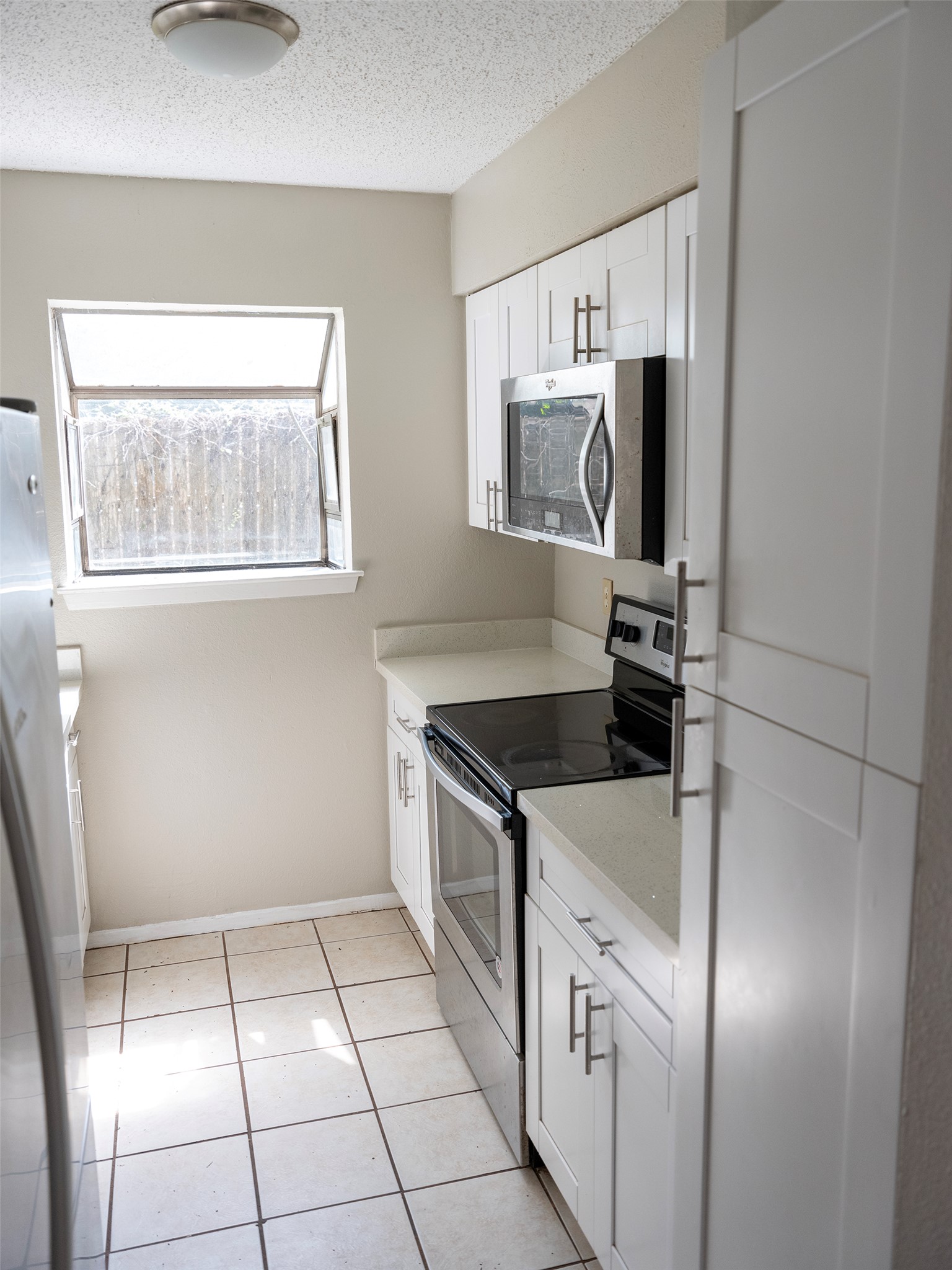 1903 West Loop, Unit B Austin, TX 78758 - Photo 13 of 15 Kitchen featuring light tile patterned flooring, a textured ceiling, white cabinets, baseboards, and appliances with stainless steel finishes