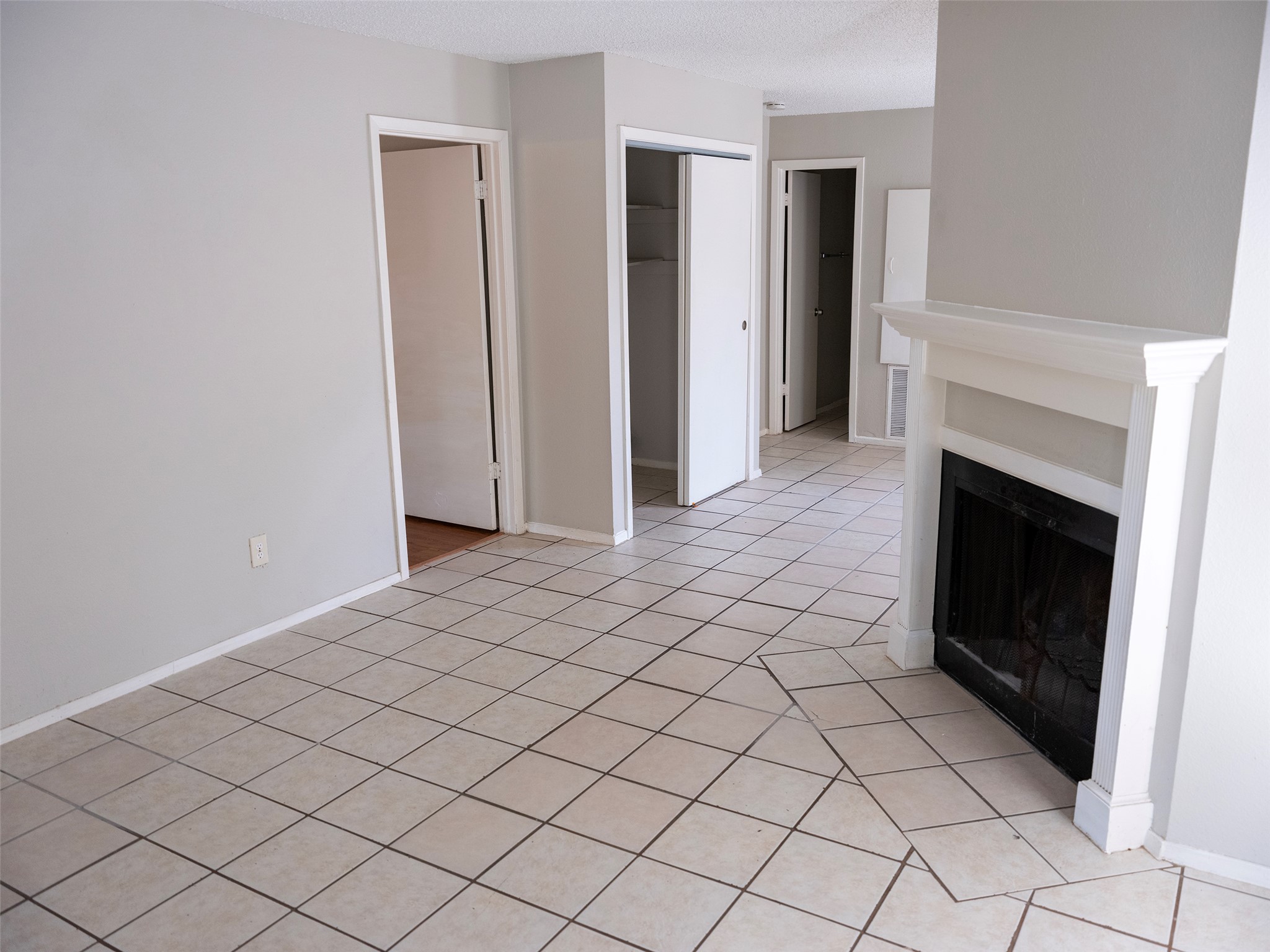 1903 West Loop, Unit B Austin, TX 78758 - Photo 2 of 15 Unfurnished living room featuring light tile patterned flooring, a textured ceiling, a fireplace, and baseboards