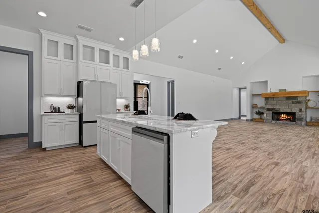 a kitchen with kitchen island granite countertop a refrigerator a sink dishwasher and white cabinets with wooden floor