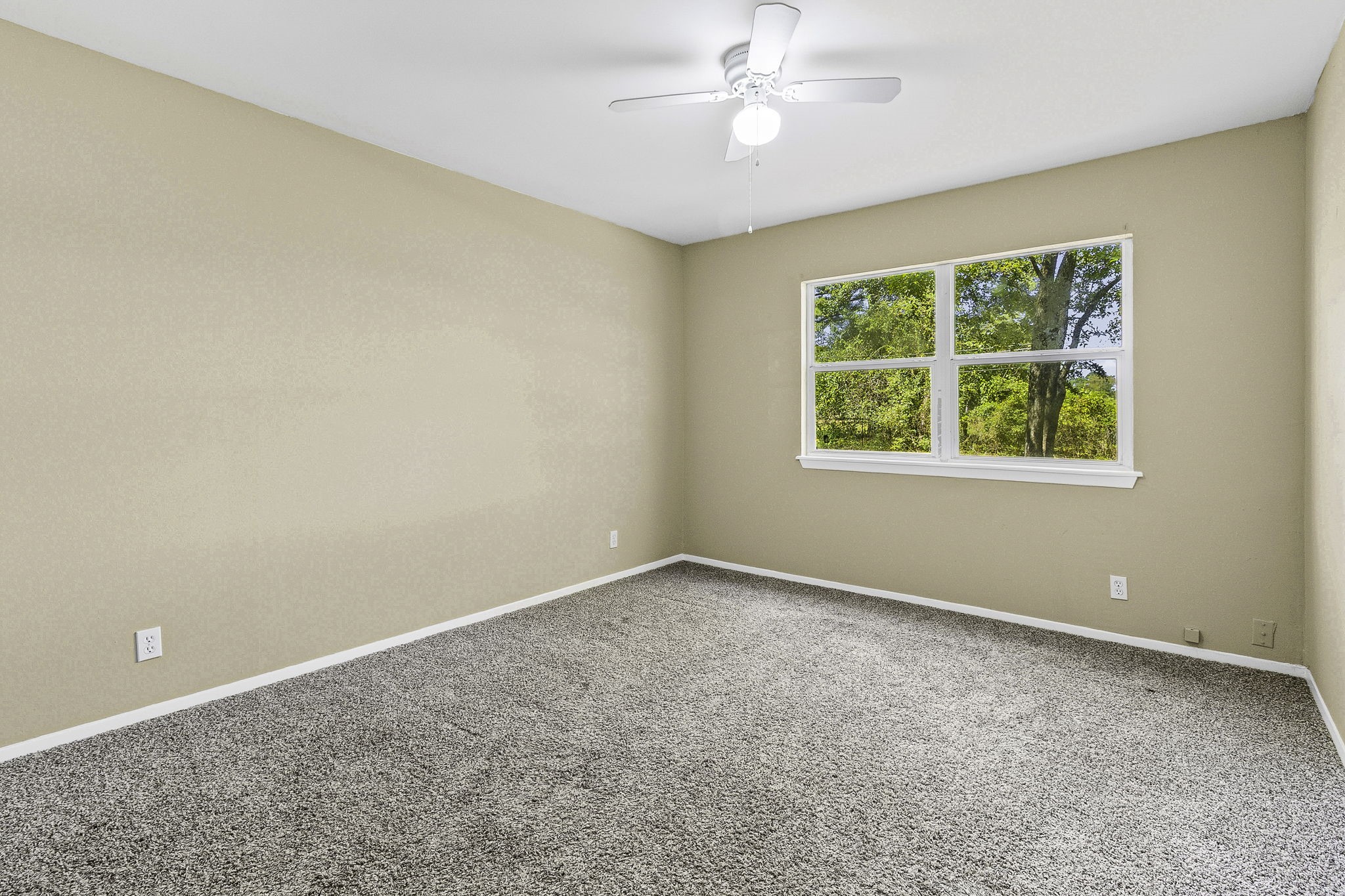 81 Westlake Road Trinity, TX 75862 - Photo 9 of 25 Bright and airy bedroom featuring neutral walls, plush carpeting, and a ceiling fan, with a window offering a serene view of lush greenery.