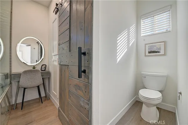a bedroom with a bed and a lamp on dresser with wooden floor