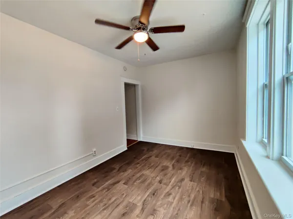 an empty room with wooden floor a ceiling fan and windows