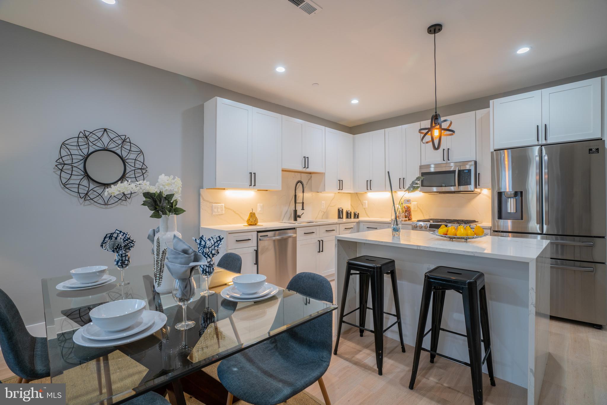 a kitchen with stainless steel appliances granite countertop a stove a refrigerator a microwave a dining table and chairs with wooden floor