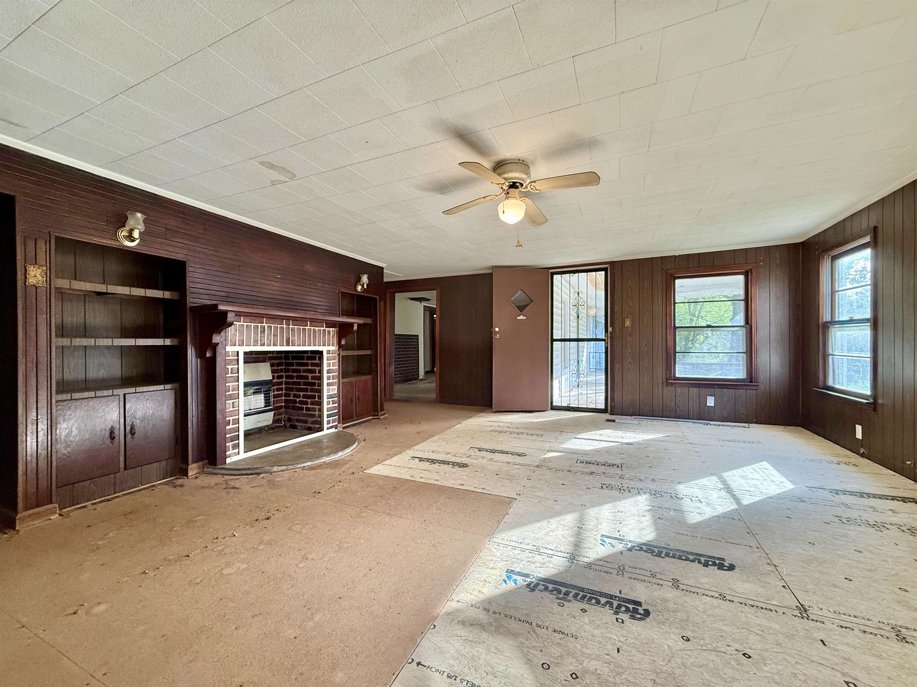 845 Needham Road Drummonds, TN 38023 - Photo 7 of 22 Unfurnished living room featuring wooden walls, a ceiling fan, and a brick fireplace