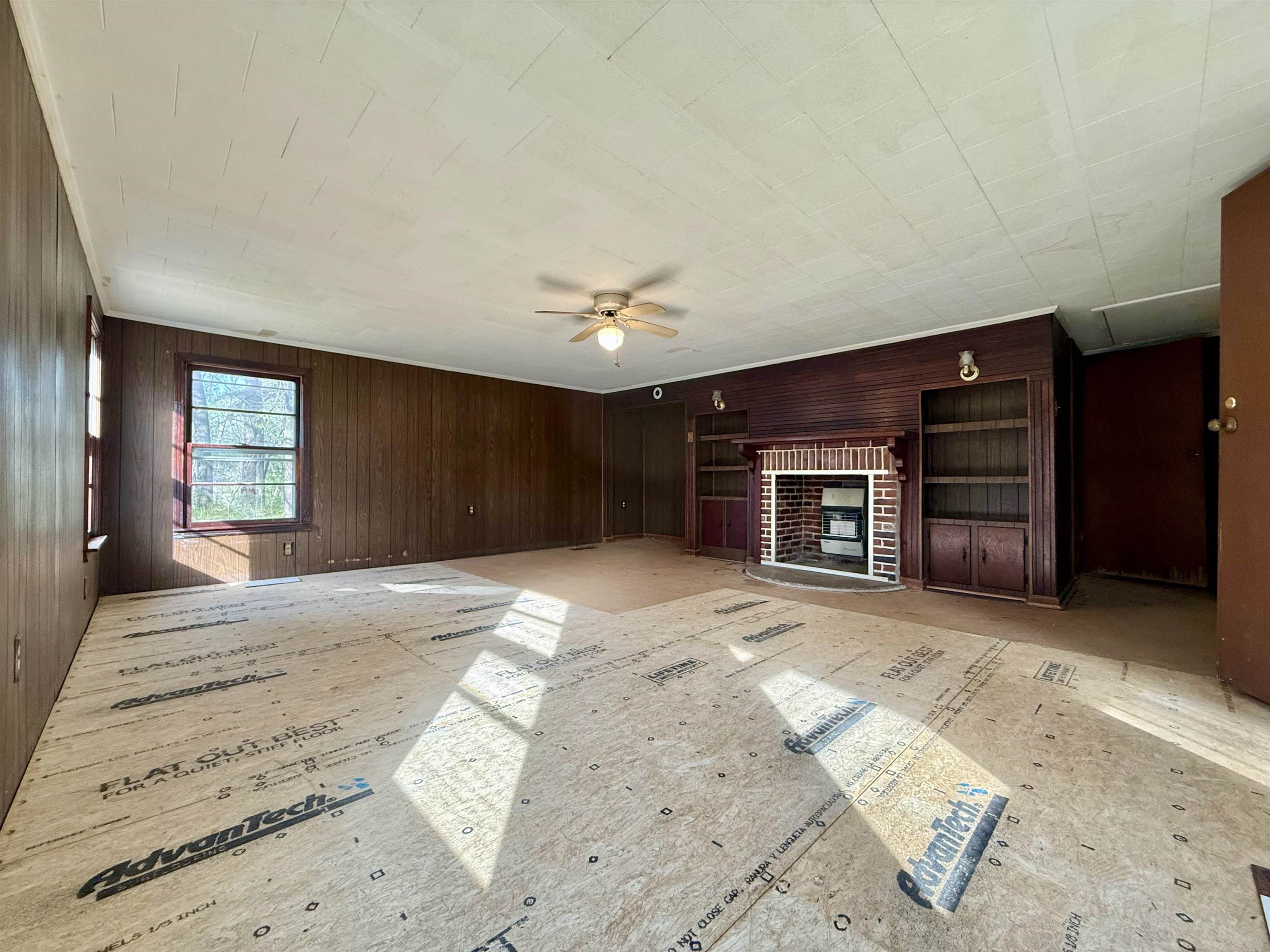 845 Needham Road Drummonds, TN 38023 - Photo 9 of 22 Unfurnished living room featuring wood walls, a fireplace, and ceiling fan