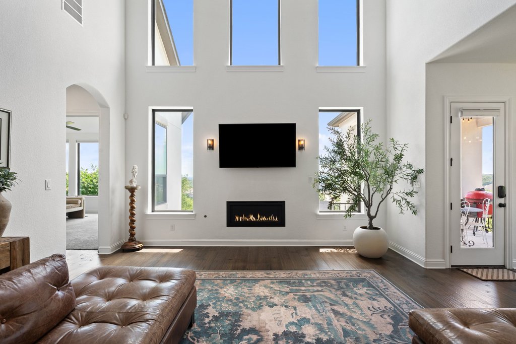 1221 Siena Sunset Road Leander, TX 78641 - Photo 10 of 39 Grand living area featuring a double-height ceiling, large rectangular windows, a built-in linear fireplace, and dark wood-finish flooring