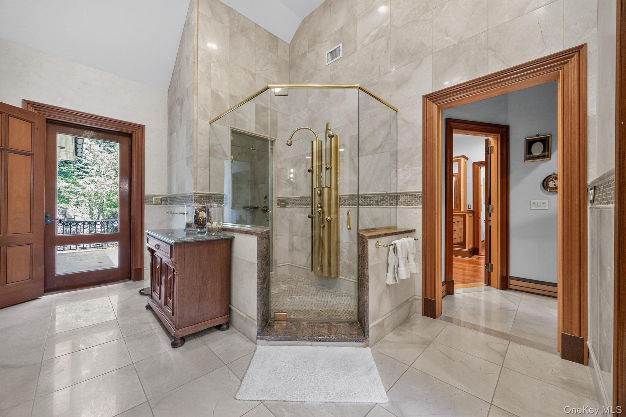 23 Inningwood Road Ossining, NY 10562 - Photo 23 of 50 Glass-enclosed shower with multiple brass fixtures, stone tile walls and flooring, a wood vanity with a stone countertop, and a wood-framed door opening to an exterior balcony
