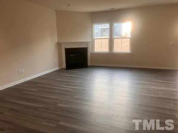 an empty room with wooden floor fireplace and windows