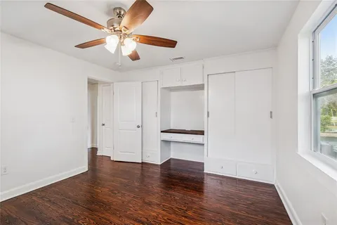 an empty room with wooden floor ceiling fan and windows
