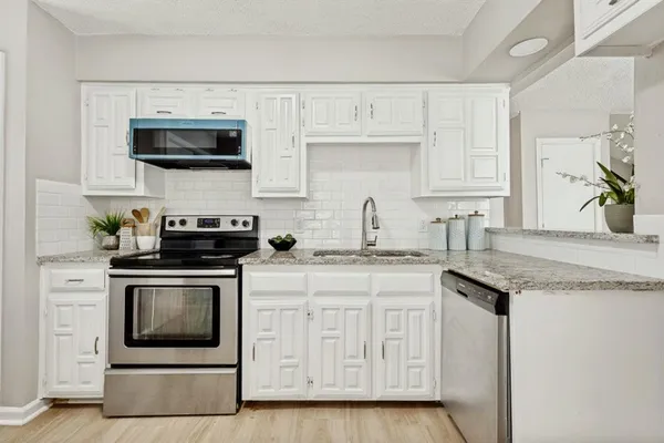 a kitchen with stainless steel appliances granite countertop white cabinets a sink and a stove