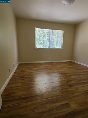a view of an empty room with wooden floor and a window