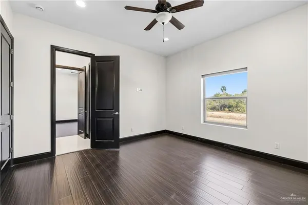 a view of an empty room with wooden floor and a ceiling fan