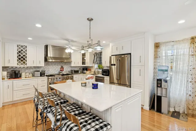 a kitchen with stainless steel appliances kitchen island granite countertop a refrigerator a stove a sink dishwasher and white cabinets with wooden floor