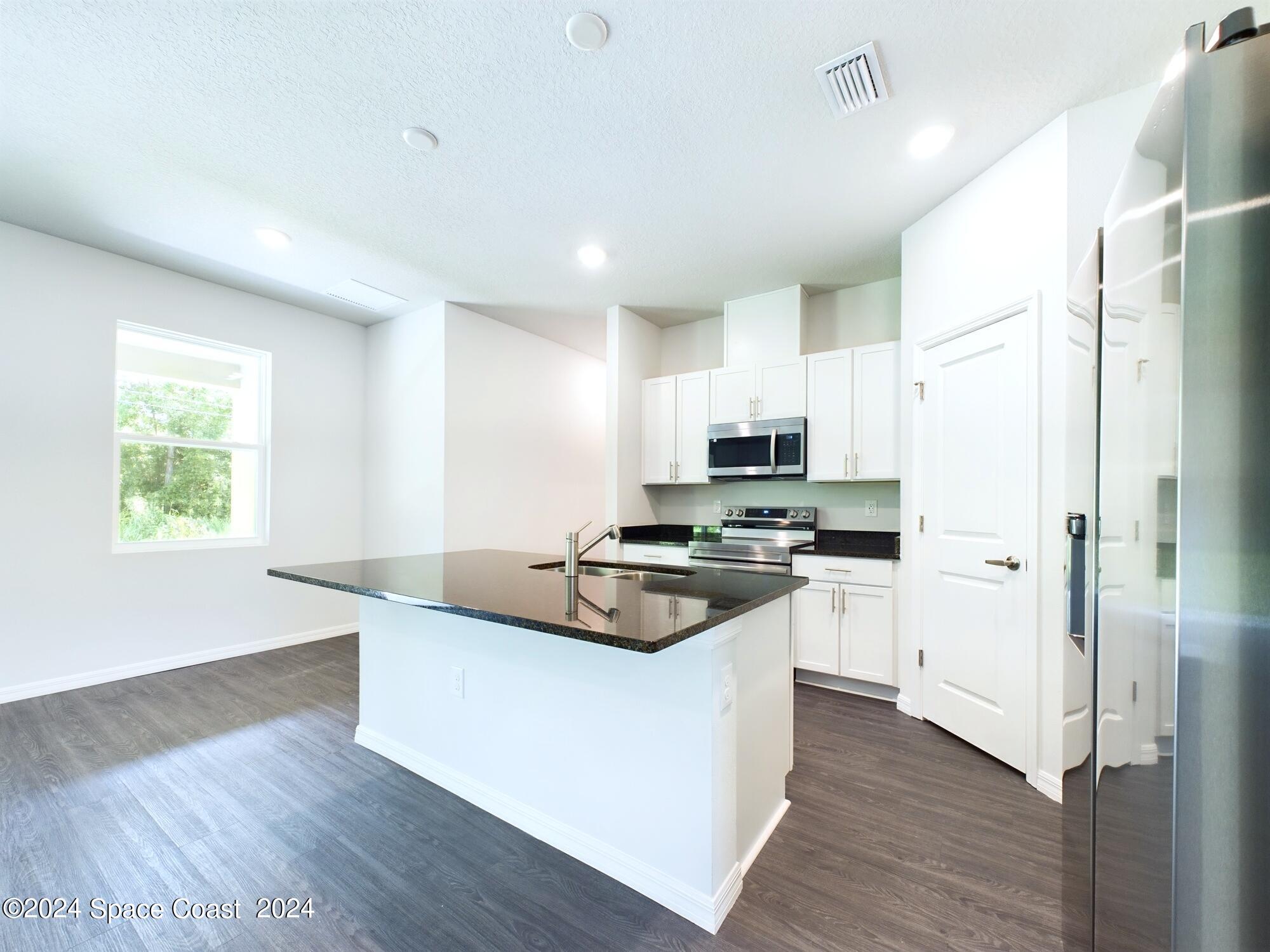 842 Angelico Road Northwest Palm Bay, FL 32907 - Photo 6 of 22 a kitchen with stainless steel appliances granite countertop a refrigerator a stove a sink and white cabinets with wooden floor