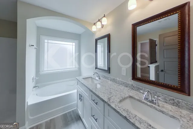 a bathroom with a granite countertop tub double vanity sink and a large mirror
