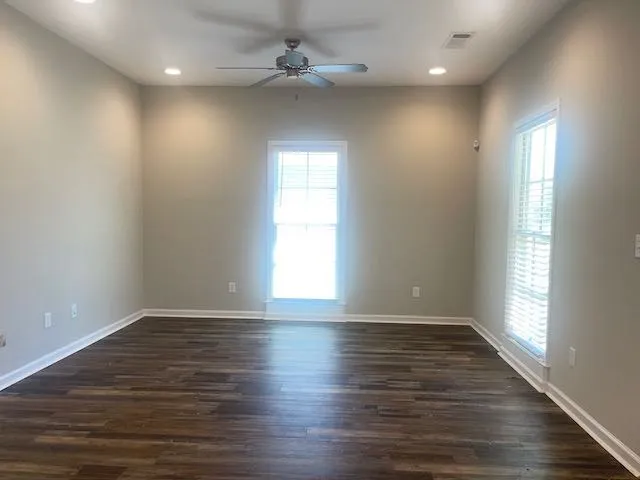 an empty room with wooden floor fan and windows