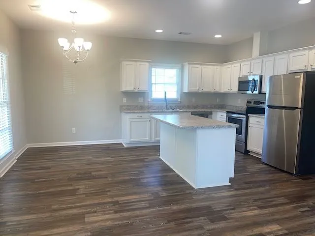 a kitchen with stainless steel appliances granite countertop a refrigerator a sink dishwasher a stove top oven a refrigerator and white cabinets with wooden floor