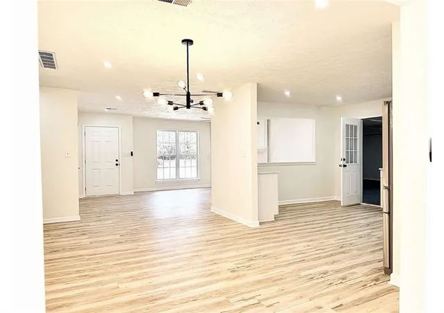 a view of an empty room and kitchen with window wooden floor