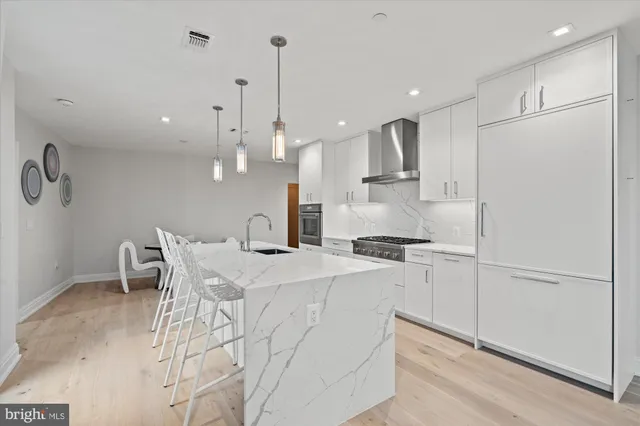 a kitchen with stainless steel appliances kitchen island granite countertop a stove a refrigerator a white table and chairs with wooden floors