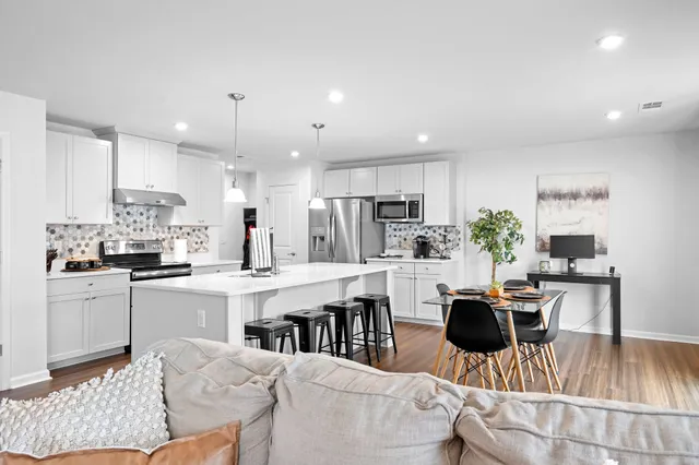 a kitchen with stainless steel appliances kitchen island granite countertop a dining table chairs refrigerator and sink