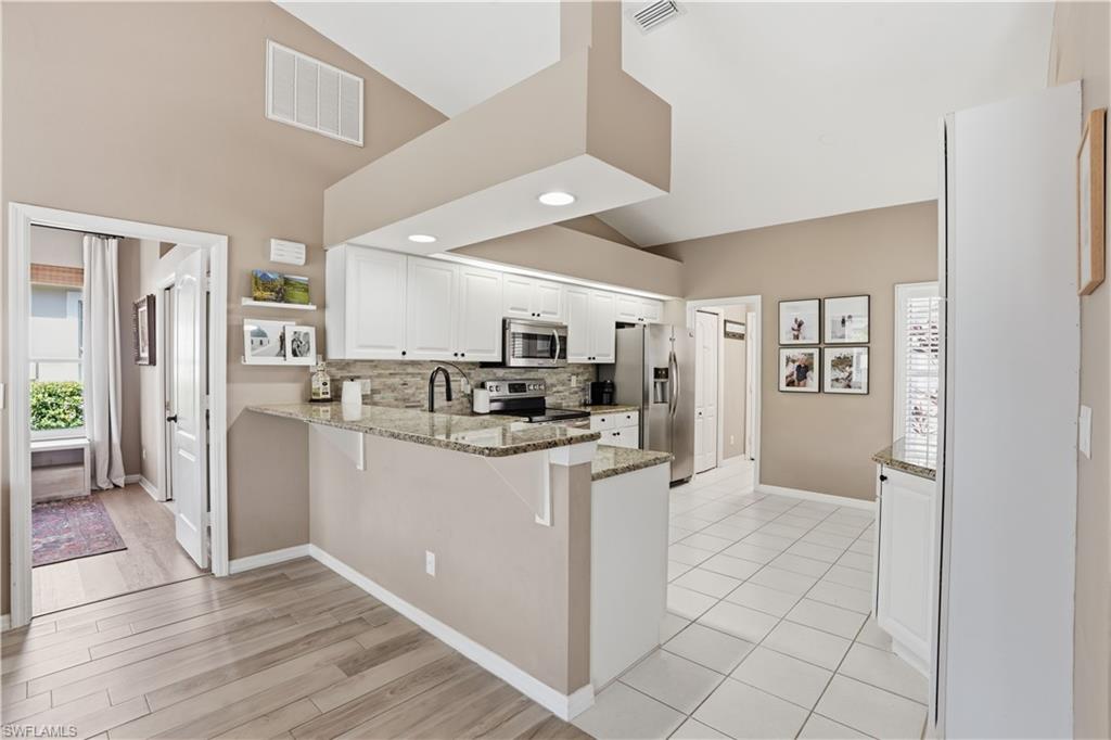 4356 Mistlethrush Lane Naples, FL 34119 - Photo 10 of 38 a kitchen with stainless steel appliances kitchen island granite countertop a refrigerator and a stove top oven