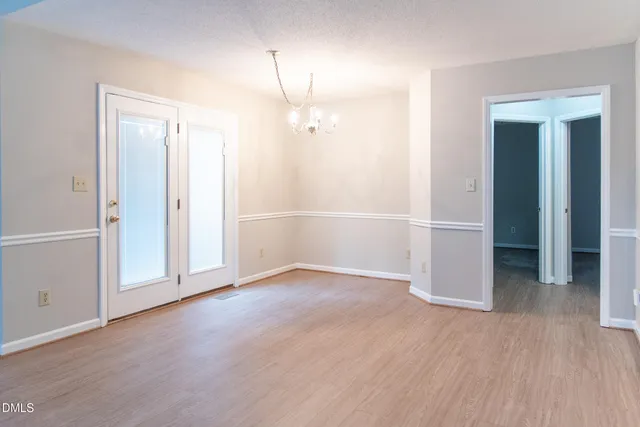 an empty room with wooden floor and way to kitchen