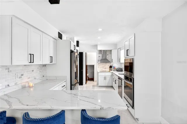 a kitchen with stainless steel appliances kitchen island granite countertop a refrigerator a stove a sink and white cabinets with wooden floor