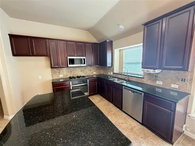 a kitchen with granite countertop wooden cabinets a stove top oven a sink and dishwasher