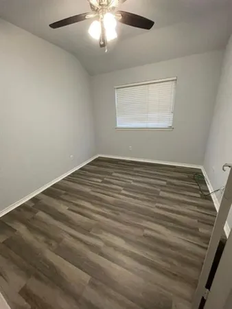 an empty room with wooden floor fan and windows
