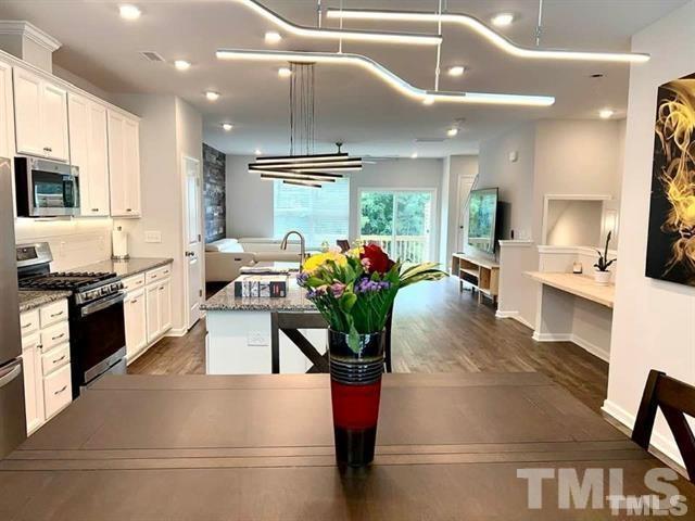 a kitchen with stainless steel appliances kitchen island granite countertop a refrigerator a sink dishwasher a oven and a dining table with wooden floor