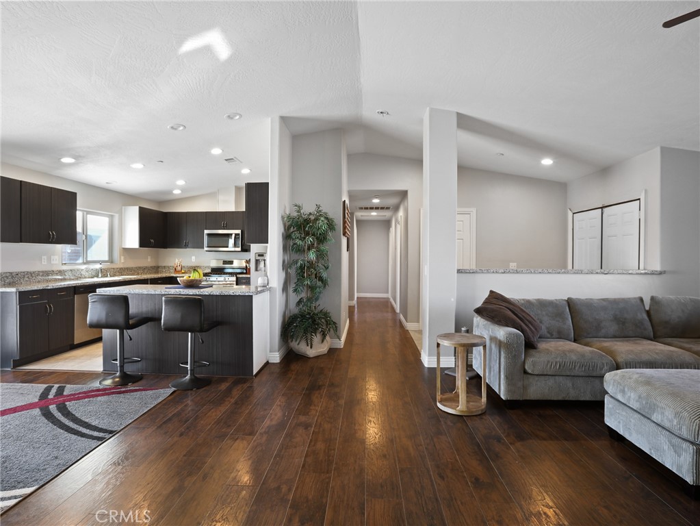a living room with stainless steel appliances furniture wooden floor and a kitchen view