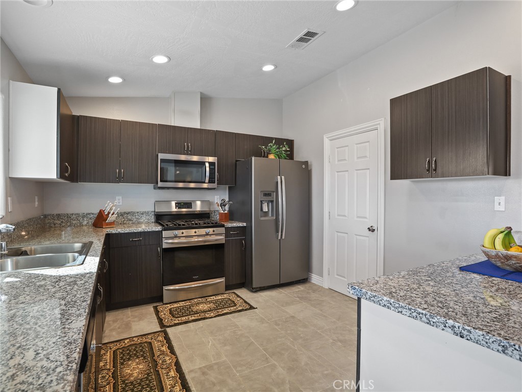 7755 7th Street Phelan, CA 92371 - Photo 8 of 27 a kitchen with granite countertop a refrigerator and a stove top oven