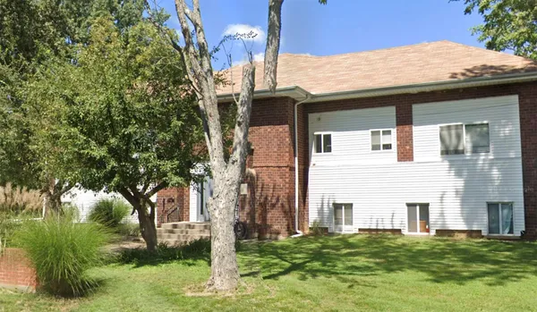a view of a white house next to a yard with big trees