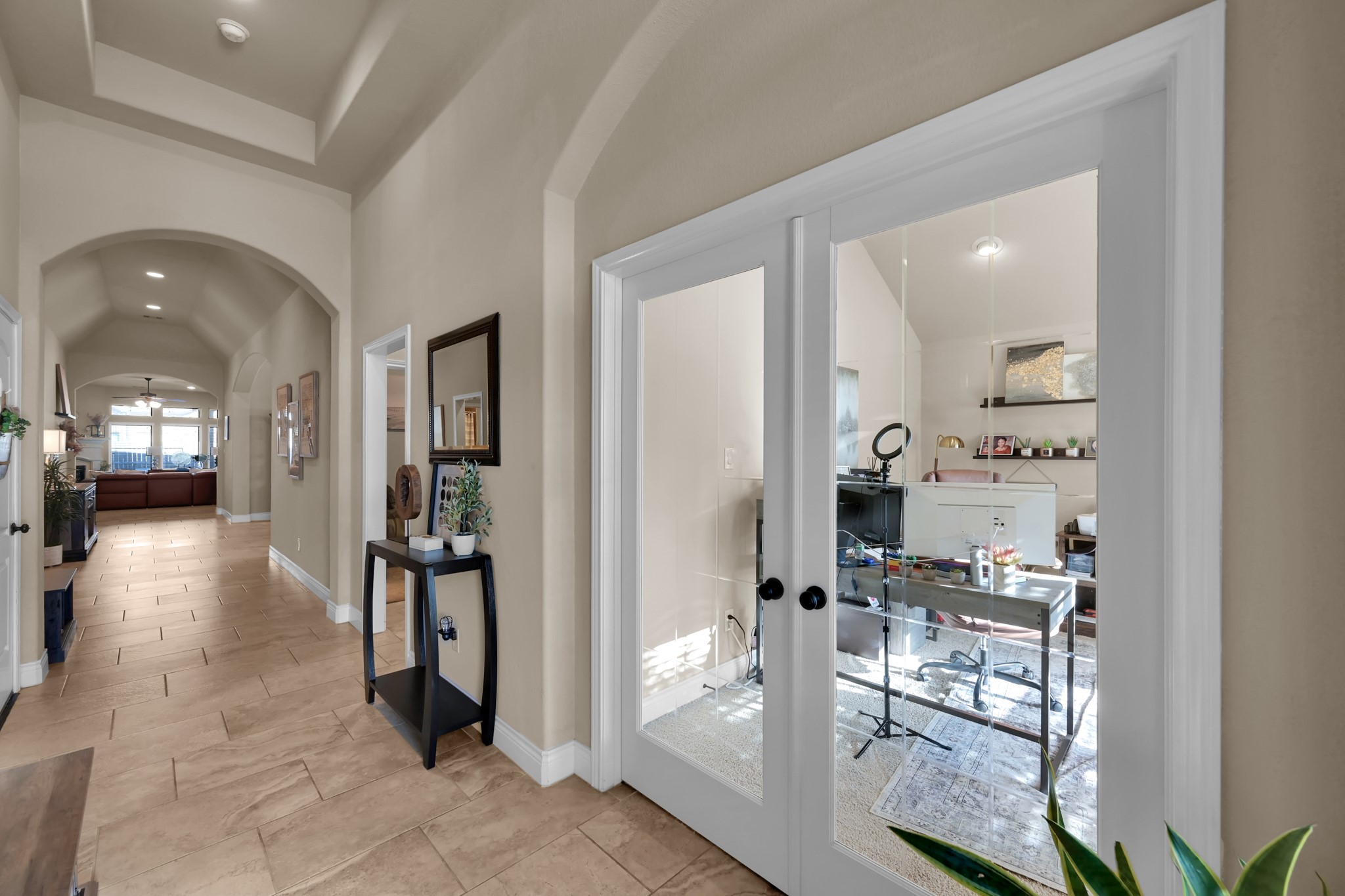 3814 Trophy Ridge Spring, TX 77386 - Photo 5 of 39 This photo showcases a spacious hallway with elegant arches and tiled flooring. To the right, there are glass double doors leading to a bright office space. The hallway leads to an open living area with large windows, creating a warm and inviting atmosphere.
