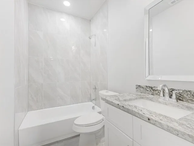 a bathroom with a granite countertop sink a toilet a mirror and bathtub