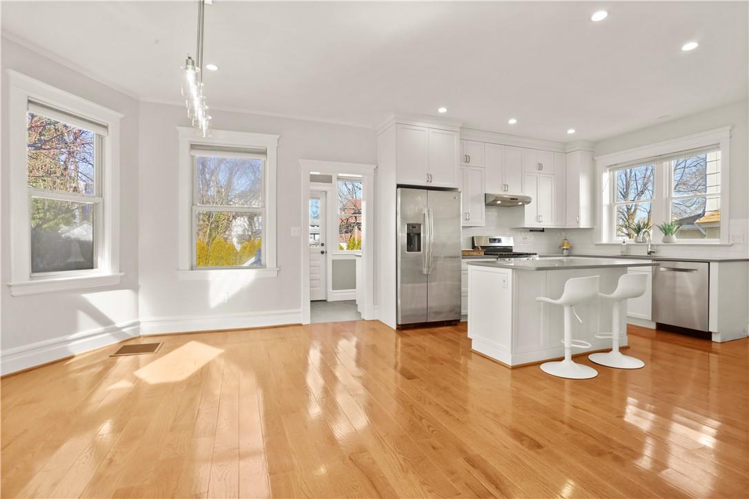 a large white kitchen with stainless steel appliances granite countertop a stove a sink a refrigerator and white cabinets with wooden floor