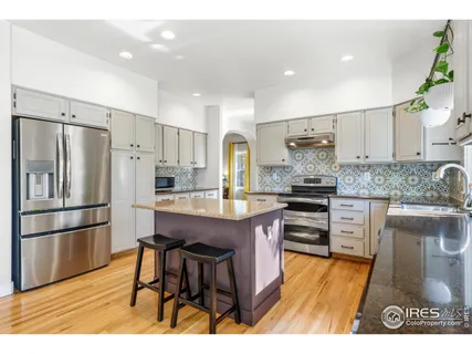 a kitchen with stainless steel appliances granite countertop a refrigerator a stove a sink dishwasher and white cabinets with wooden floor