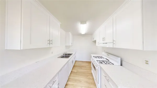 a kitchen with granite countertop a sink a stove and white cabinets with wooden floor