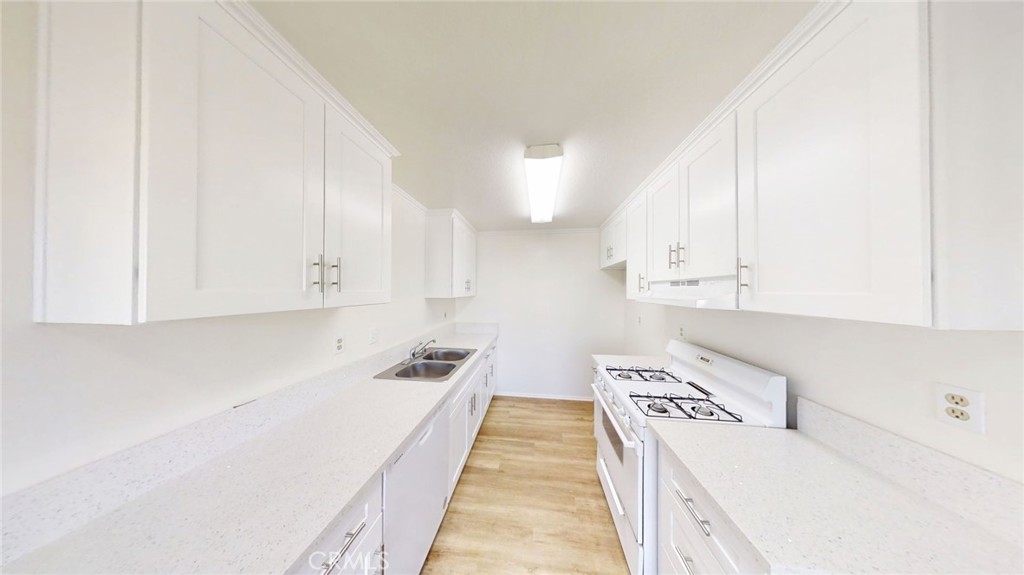 13475 4th Street, Unit 5 Yucaipa, CA 92399 - Photo 6 of 10 a kitchen with granite countertop a sink a stove and white cabinets with wooden floor