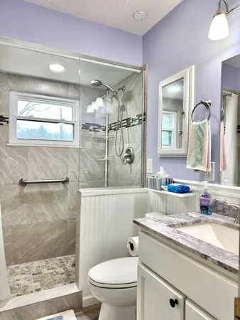a bathroom with a granite countertop sink a toilet a mirror and shower
